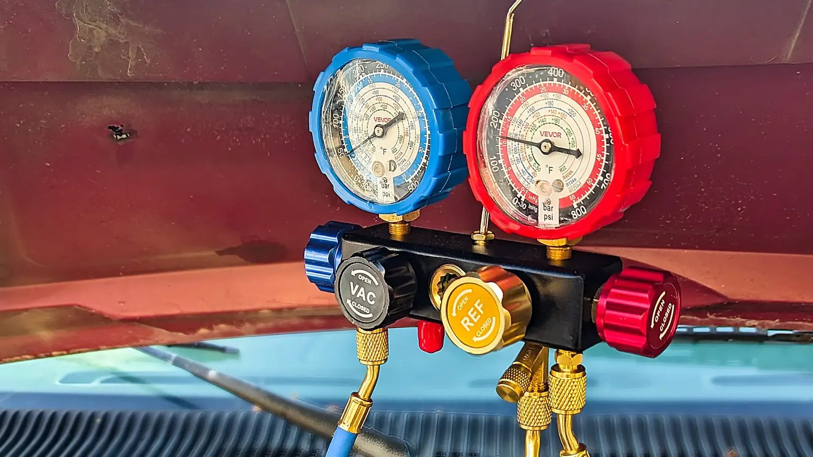 AC manifold gauges hung from the hood of a Ford Econoline during an on-site repair