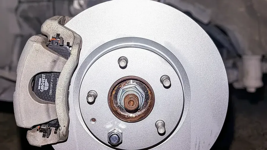 Brake caliper with pads mounted over a new rotor on a car with the wheel removed