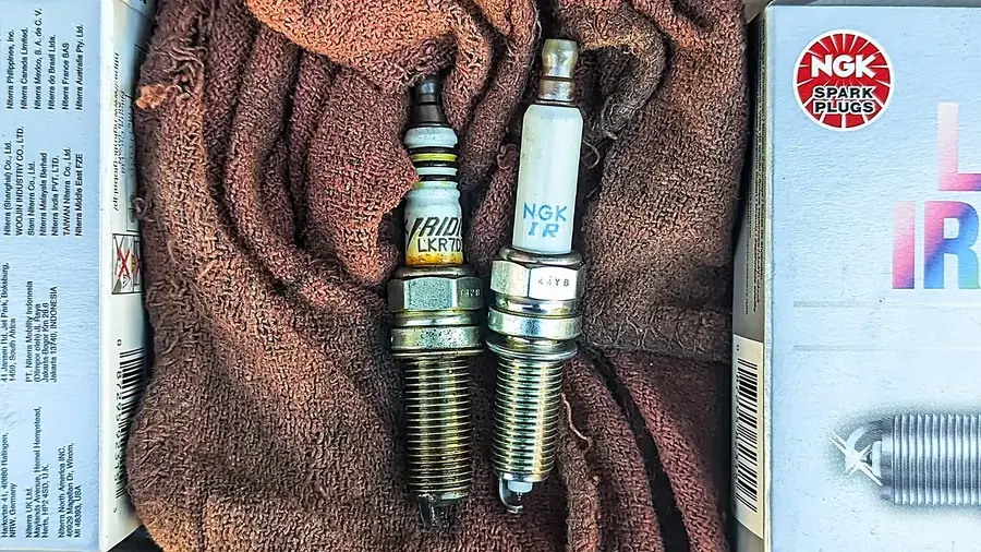 Worn spark plug next to a new NGK iridium plug, a common fix for misfire codes that fail an emissions test