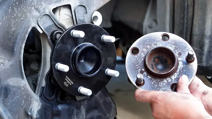Mechanic swapping a worn wheel hub for a new one, with the strut and coil spring visible
