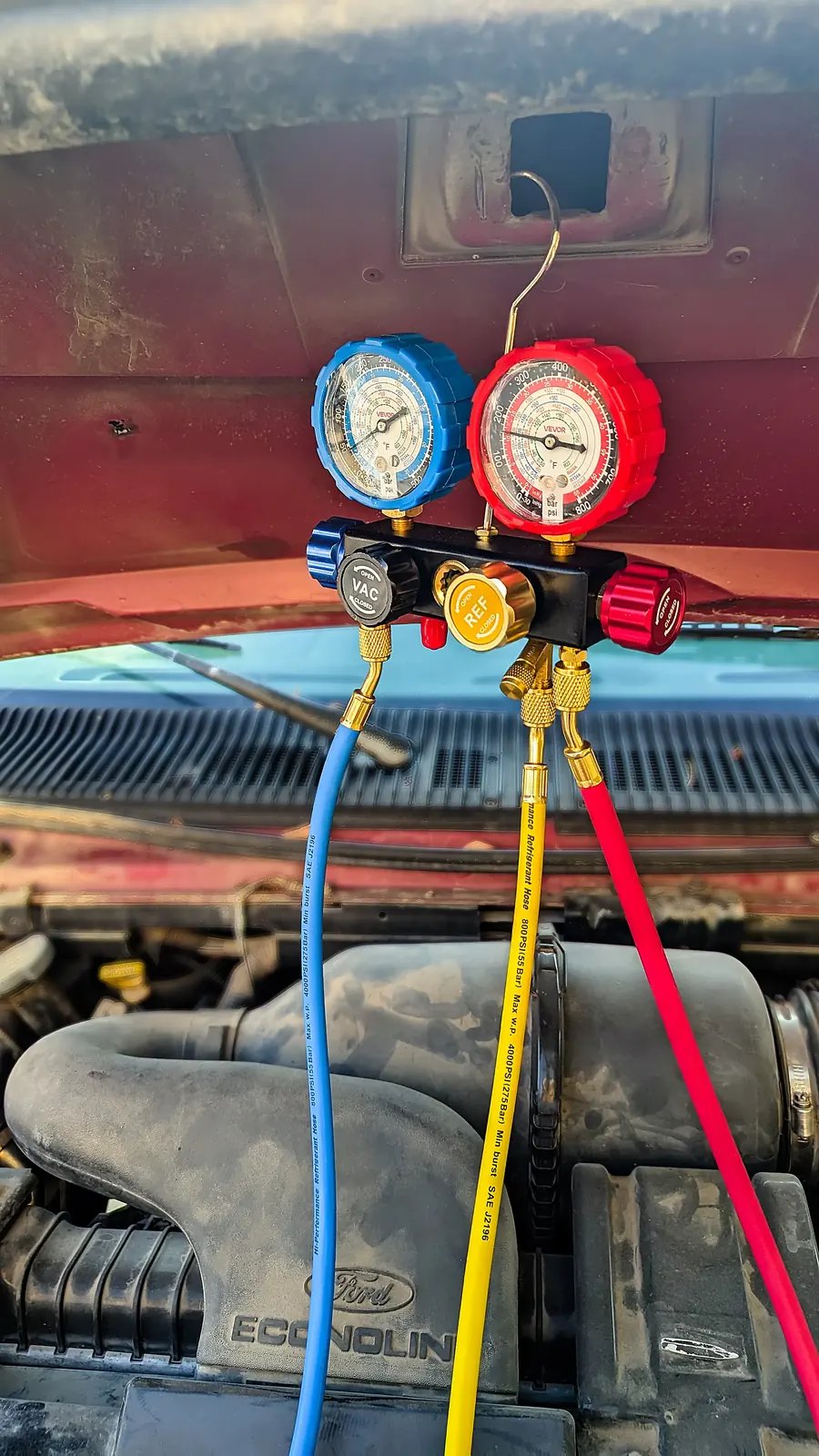 AC manifold gauges hung from the hood of a Ford Econoline during a mobile AC repair