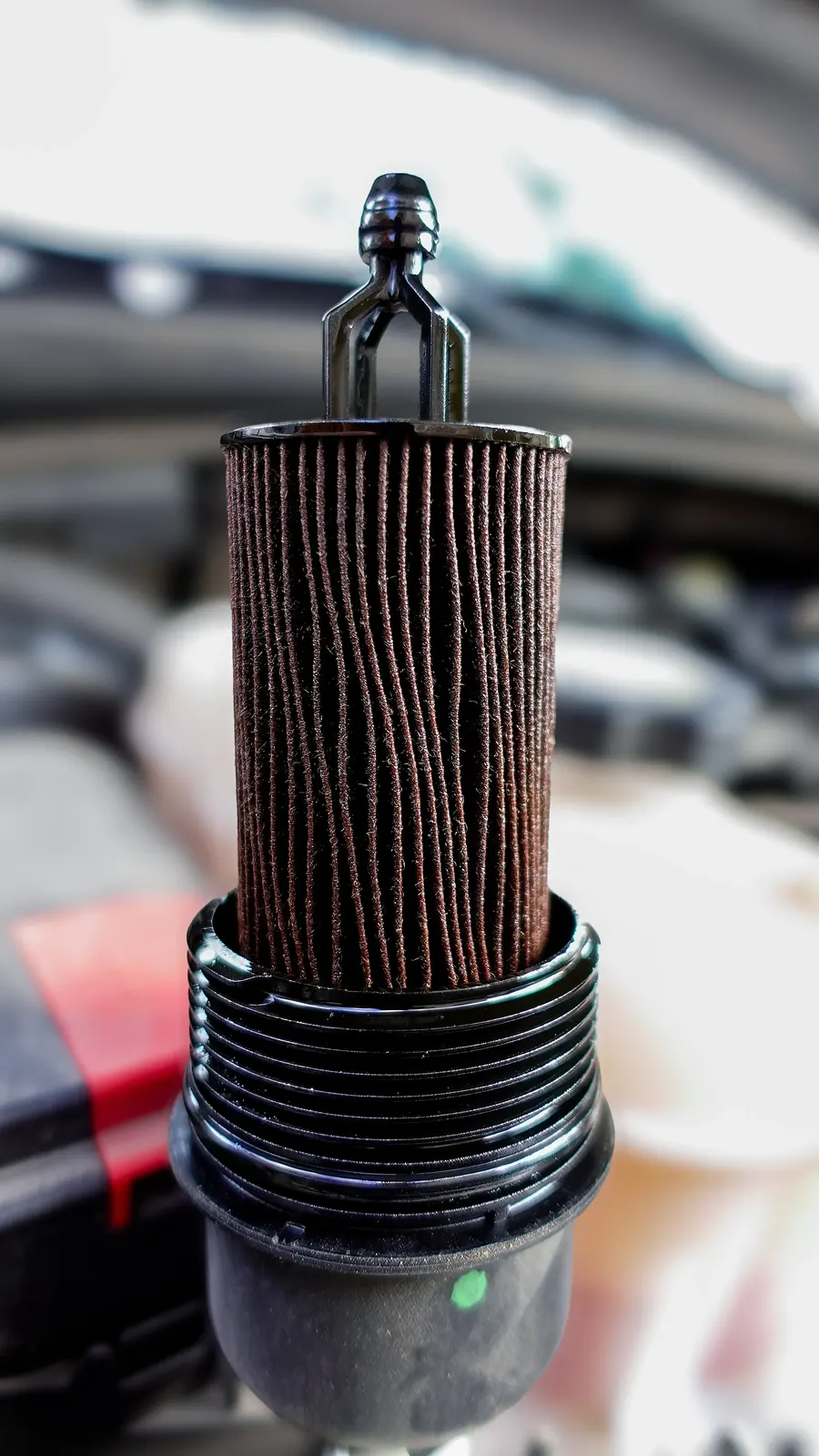 Used cartridge oil filter element held up over the engine bay during a mobile oil change