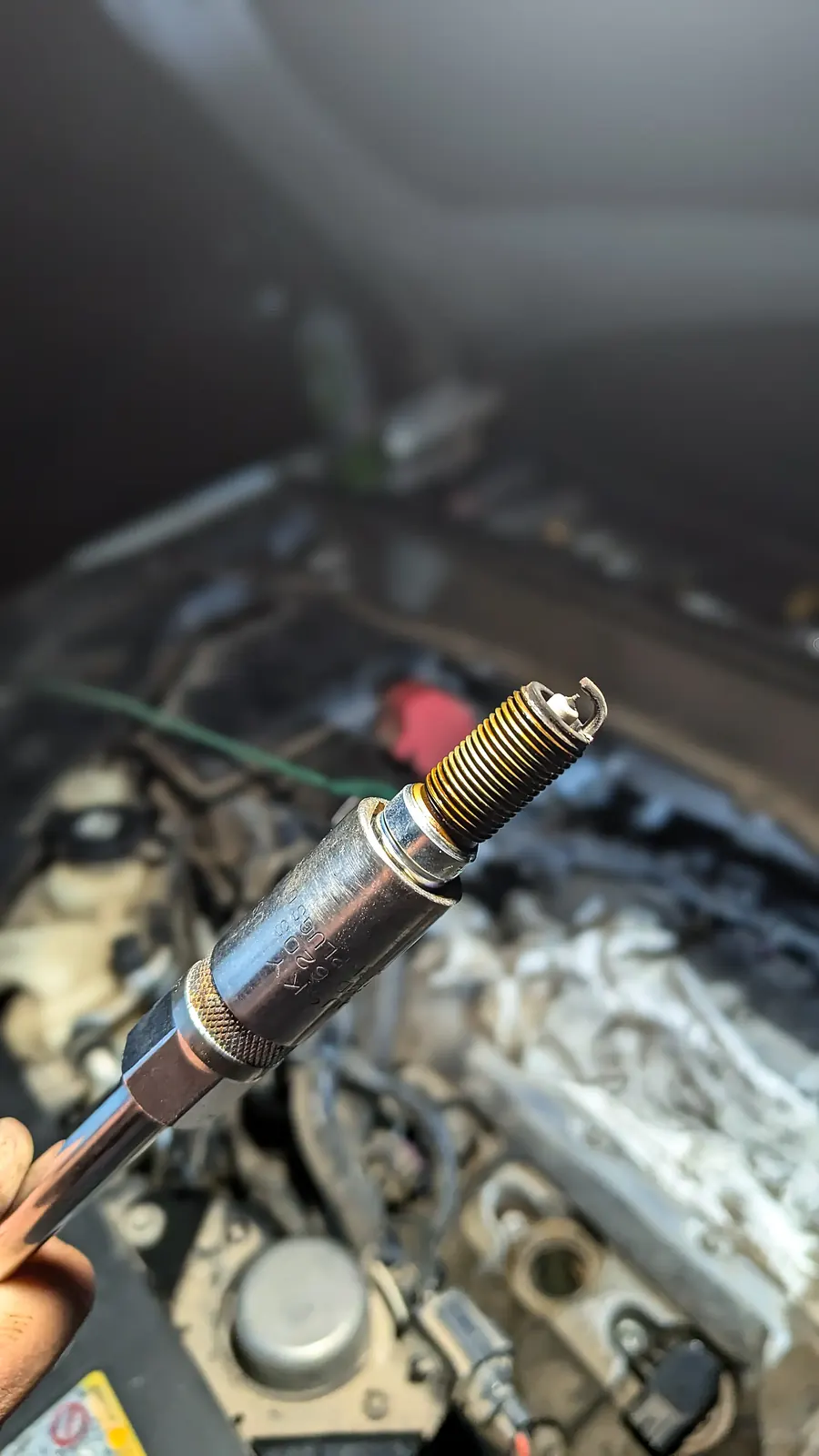 Worn spark plug coming out of the engine on a spark plug socket